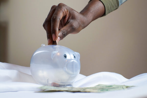 A hand placing a coin in a translucent piggy bank.