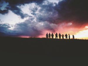 A line of people silhouetted against a sunset.